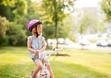 Girl in pink helmet sitting on her bike in a sunny city park