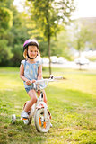 Girl in pink helmet sitting on her bike in a sunny city park
