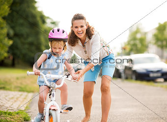 Happy mother pushes daughter on her bike as she learns to ride