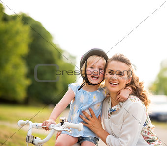 Proud girl on a bicycle hugging her mother in a city park