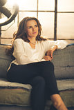 Elegant woman sitting on a sofa in a loft looking into distance