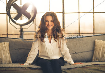 Smiling, elegant woman leaning forward sitting on sofa in loft