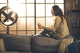 Profile shot of woman sitting on sofa back texting on phone