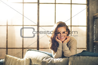 Brunette leaning over sofa smiling, resting chin on hands