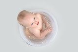 Cute baby having a bath in transparent bucket and playing