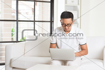 Southeast Asian male using internet at home, sitting on sofa rel