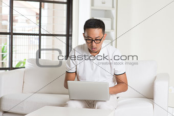 Southeast Asian male using internet at home, sitting on sofa sho