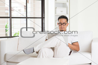 malay Asian male using internet at home, sitting on sofa relaxin