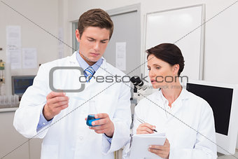 Scientists examining attentively pipette with blue fluid