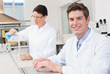 Scientist working attentively with laptop and another with beaker