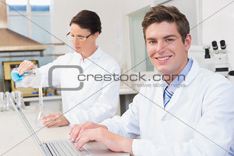 Scientist working attentively with laptop and another with beaker