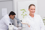 Happy scientist smiling at camera showing plant
