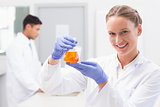 Smiling scientist looking at camera and holding beaker with orange fluid