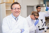 Smiling scientist looking at camera while colleagues working with microscope