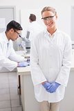 Smiling scientist looking at camera while colleagues working behind