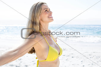 Smiling pretty blonde standing by the sea arms outstretched