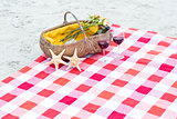 Picnic basket with glasses of red wine and starfishes on a blanket