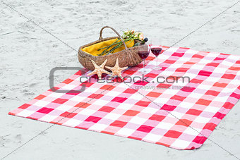 Picnic basket with glasses of red wine and starfishes on a blanket