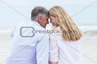 Happy couple sitting on the sand and smiling at each other