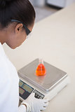 Scientist weighing beaker with orange fluid inside
