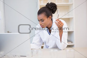 Scientist holding test tube while using laptop