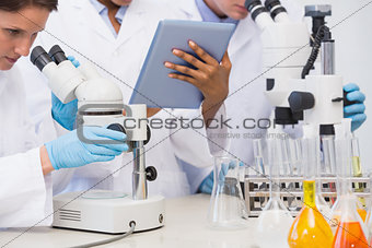 Scientists working with microscope and tablet