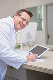 Smiling scientist holding tablet writing on notebook
