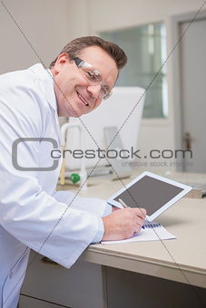 Smiling scientist holding tablet writing on notebook