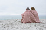 Happy couple sitting on the sand with blanket around them