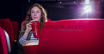 Young woman watching a film and drinking a soda