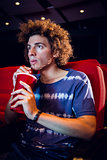 Young man watching a film and drinking soda