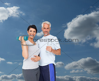 Composite image of happy fit couple with dumbbell and water bottle