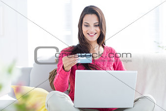 Smiling beautiful brunette doing online shopping on the couch