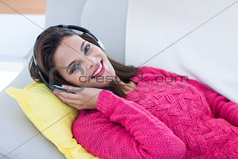Smiling beautiful brunette relaxing on the couch and listening music