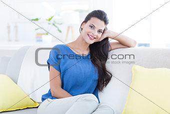 Smiling beautiful brunette relaxing on the couch and looking at camera