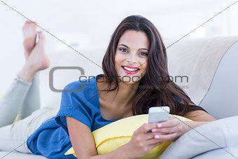 Smiling beautiful brunette relaxing on the couch and using her phone