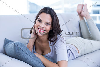 Smiling beautiful brunette relaxing on the couch and looking at camera
