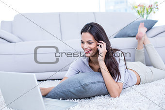 Smiling beautiful brunette lying on the floor and speaking on the phone