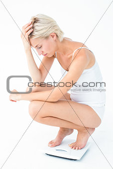 Sad woman squatting on scales