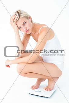 Sad woman squatting on scales looking at camera