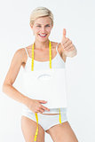 Happy woman holding scales with thumbs up