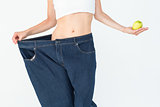 Slim woman wearing too big jeans holding an apple