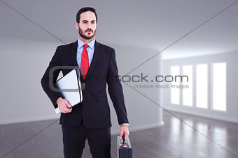 Composite image of handsome businessman holding briefcase and laptop