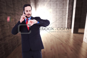 Composite image of serious businessman checking the time while on the phone