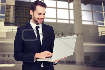 Composite image of smiling businessman standing and using laptop