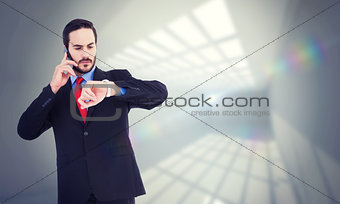 Composite image of serious businessman checking the time while on the phone