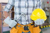 Composite image of handyman holding hammer and hard hat