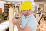 Composite image of carpenter using measure tape to mark on wooden plank