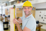 Composite image of construction worker using measure tape to mark on plank