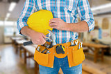 Composite image of manual worker wearing tool belt while holding hammer and helmet